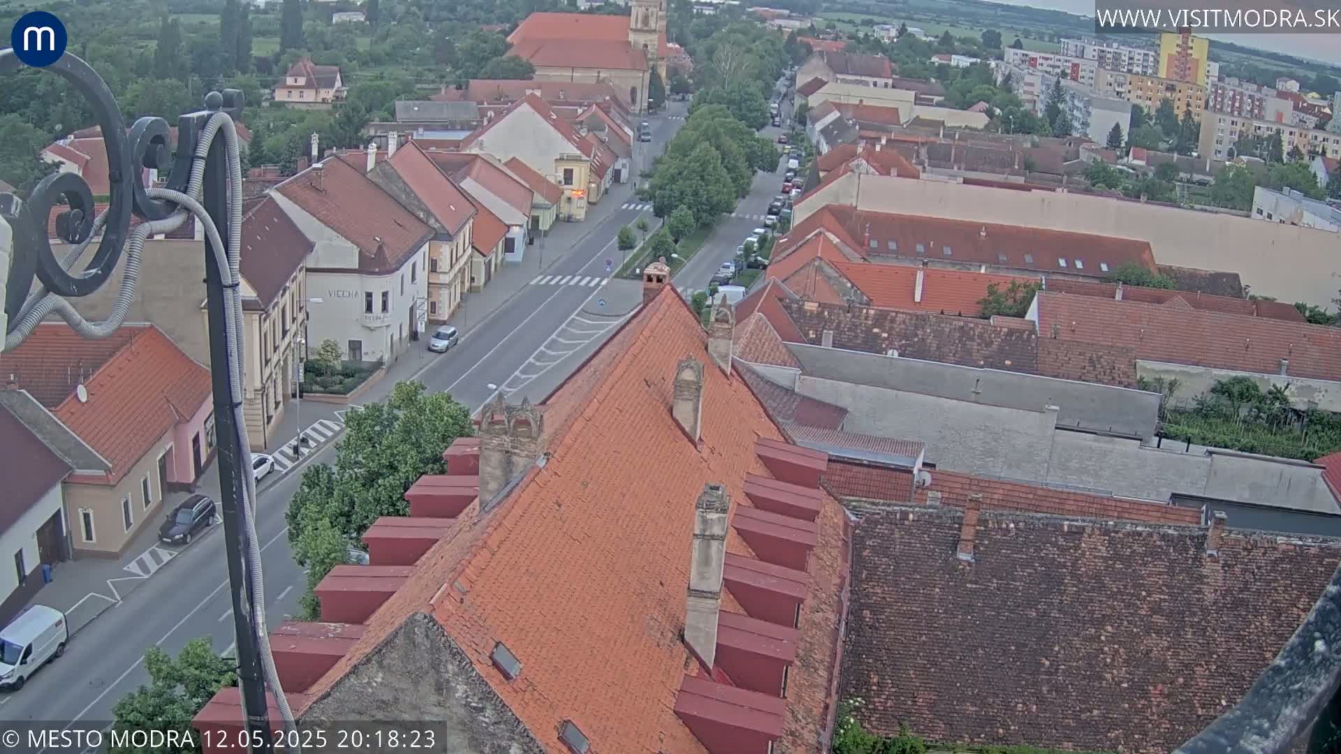 An elevated view shows a town with red-tiled roofs under a twilight sky.