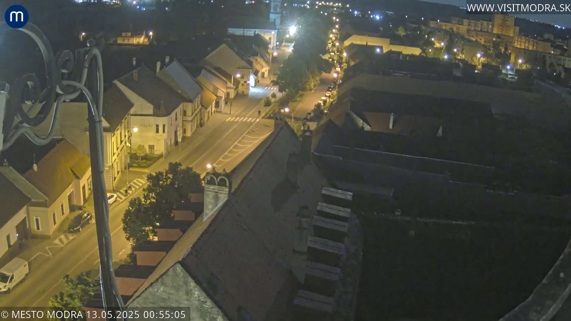A nighttime, high-angle view shows a street lined with buildings, lit by streetlights, in a town.