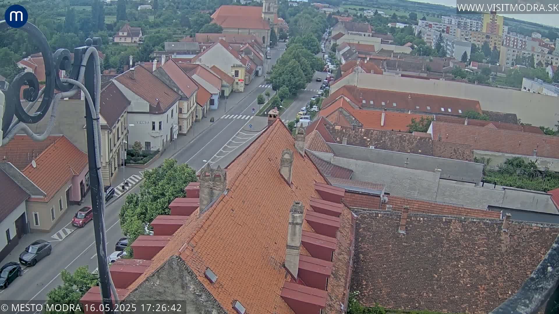An overcast view of a town's red-tiled rooftops and streets, with cars visible on a road that runs through the center.