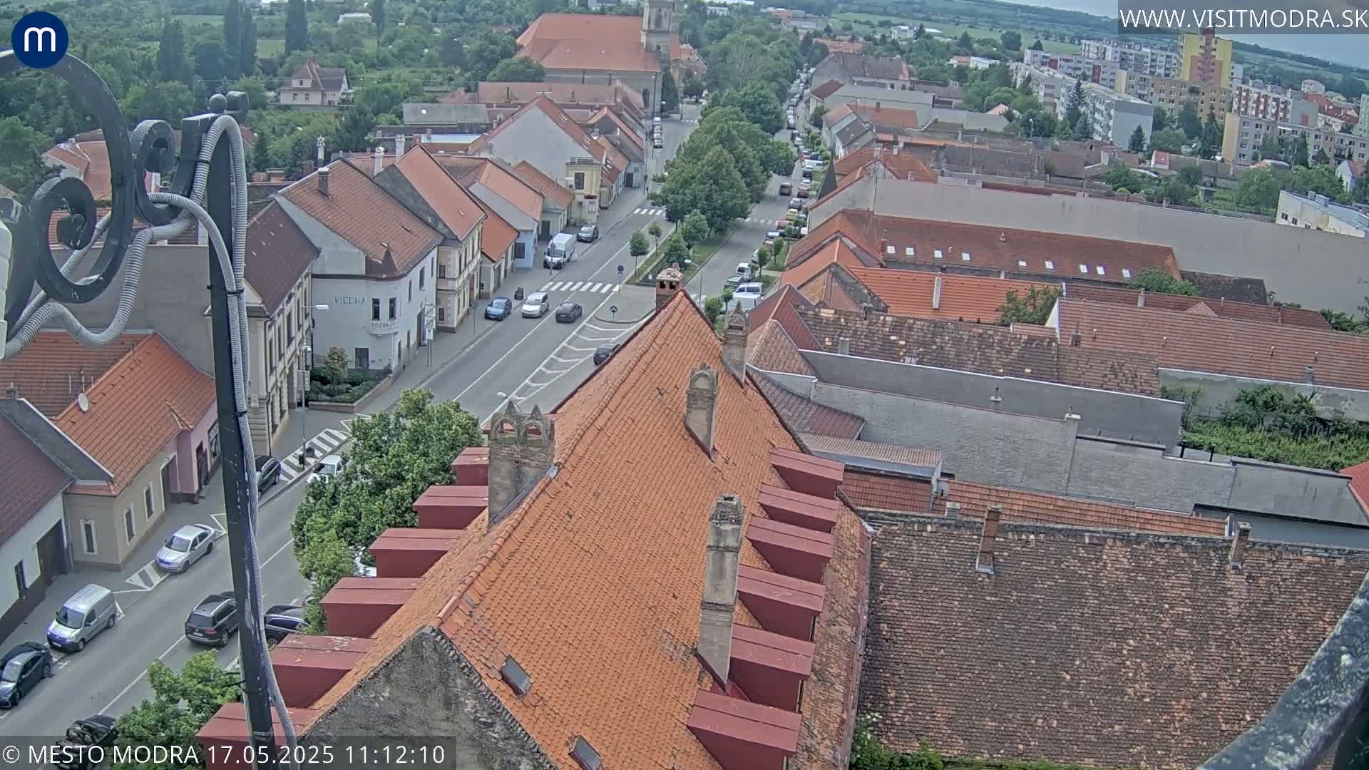 An elevated view of a town on an overcast day, showing a street with cars and buildings with red tile roofs.