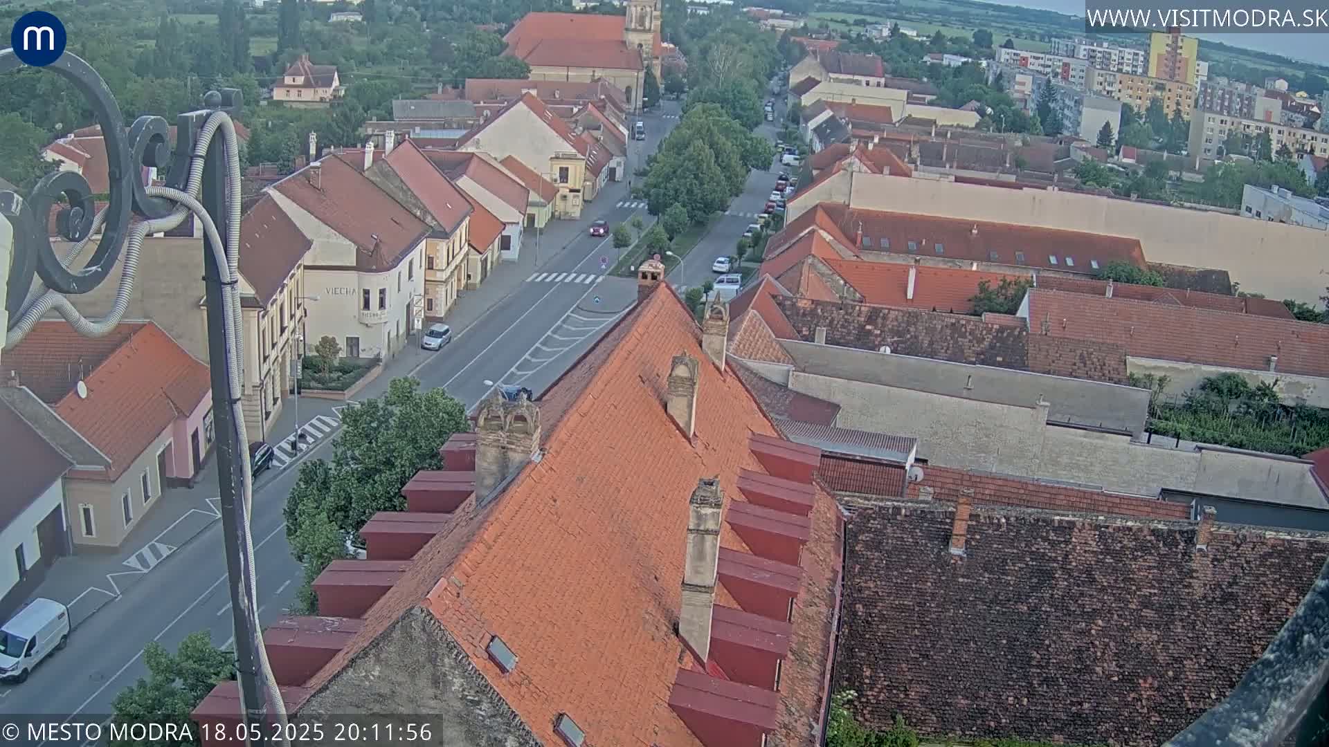 An aerial view of a town with red-tiled roofs and a street lined with buildings, under an overcast sky.