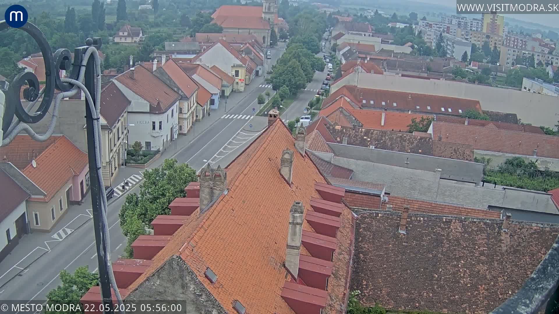 An elevated view of a town on an overcast day, showing a street lined with buildings with red tile roofs.