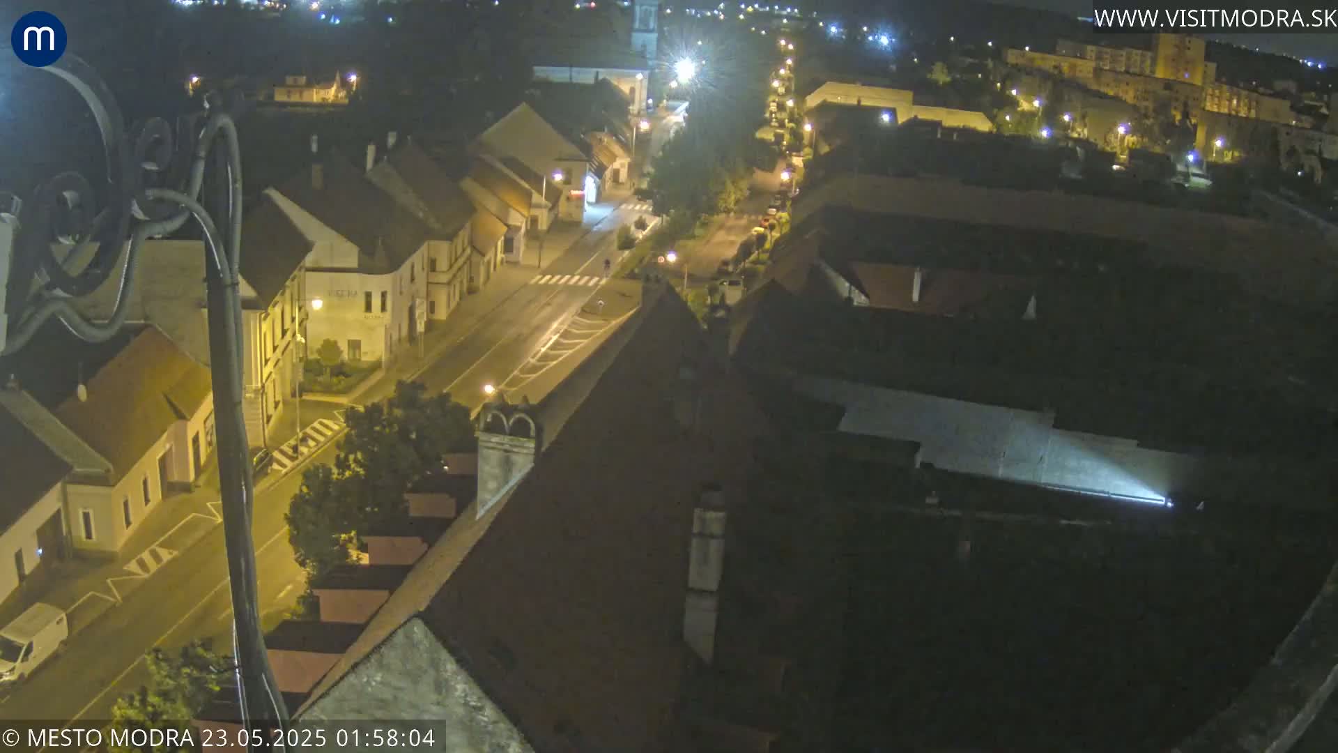 An aerial nighttime view shows a town's street scene with buildings illuminated by streetlights.