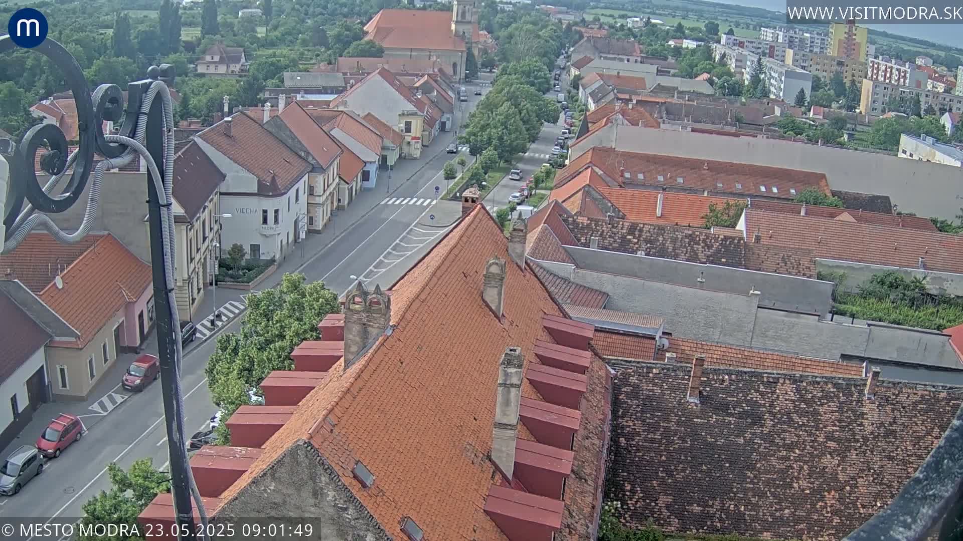 An overcast day view of a town's rooftops and streets, showing a mix of older and newer buildings with cars parked along the roads.