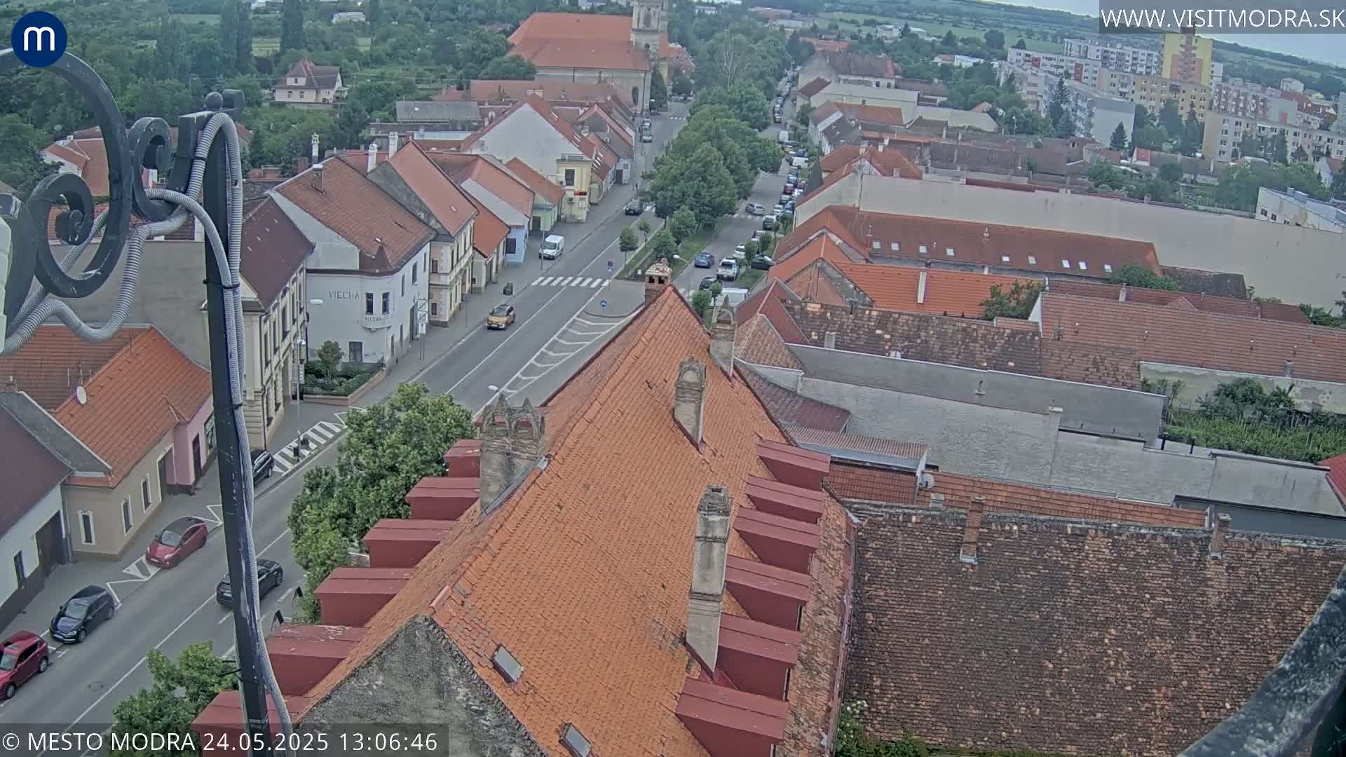 An overcast view of a town's rooftops and streets, showing several cars parked and driving on the road.