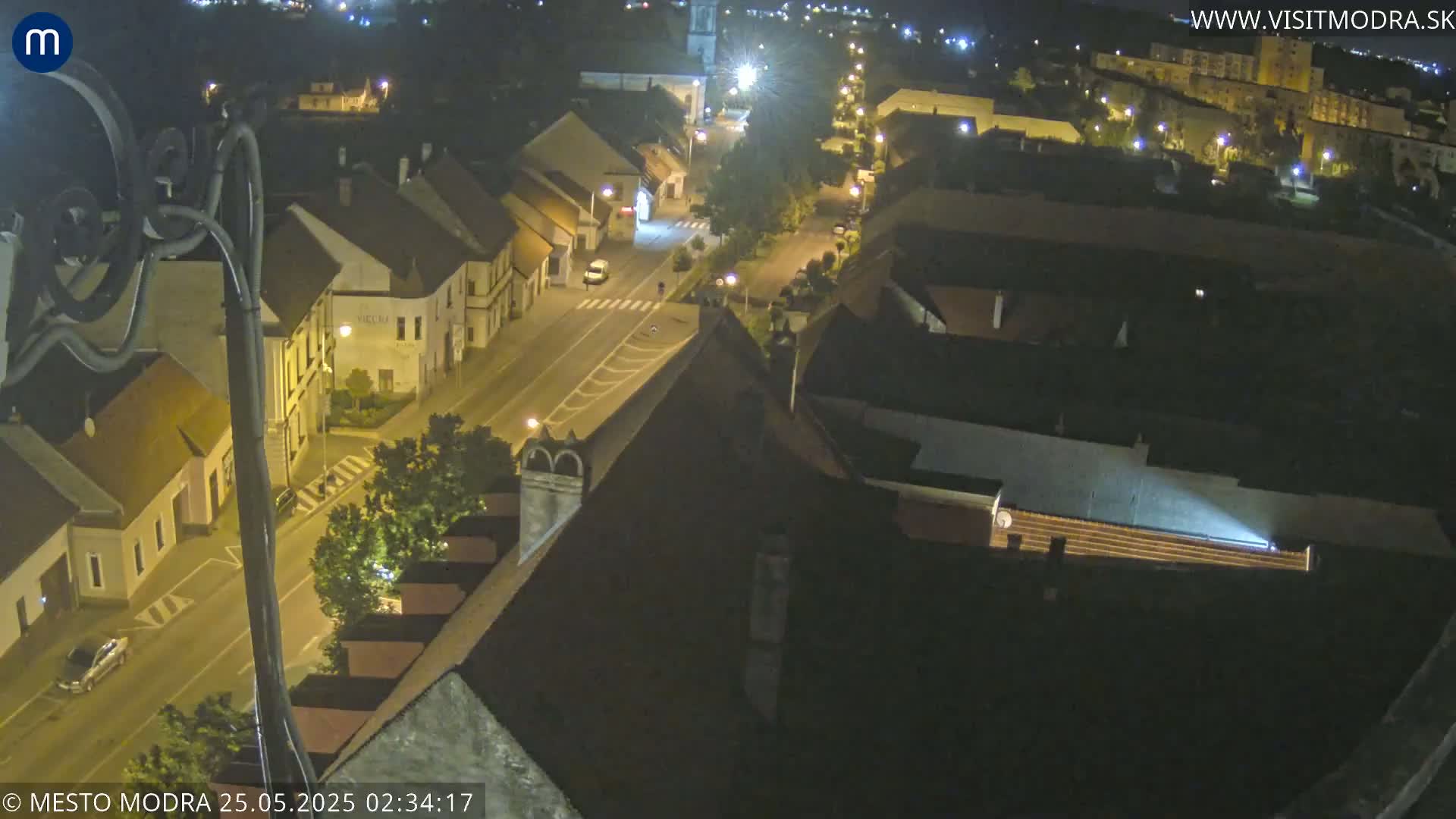 An aerial nighttime view shows a town with streets lined with buildings, illuminated by streetlights.