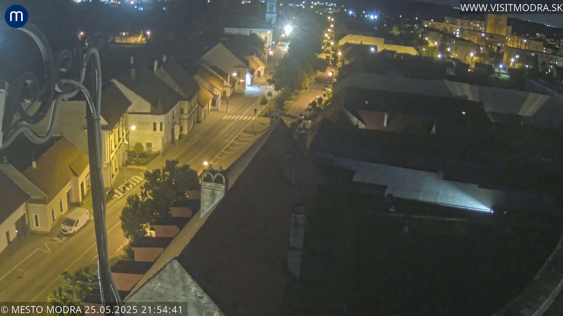 A nighttime high-angle view of a town's streets and buildings, illuminated by streetlights.