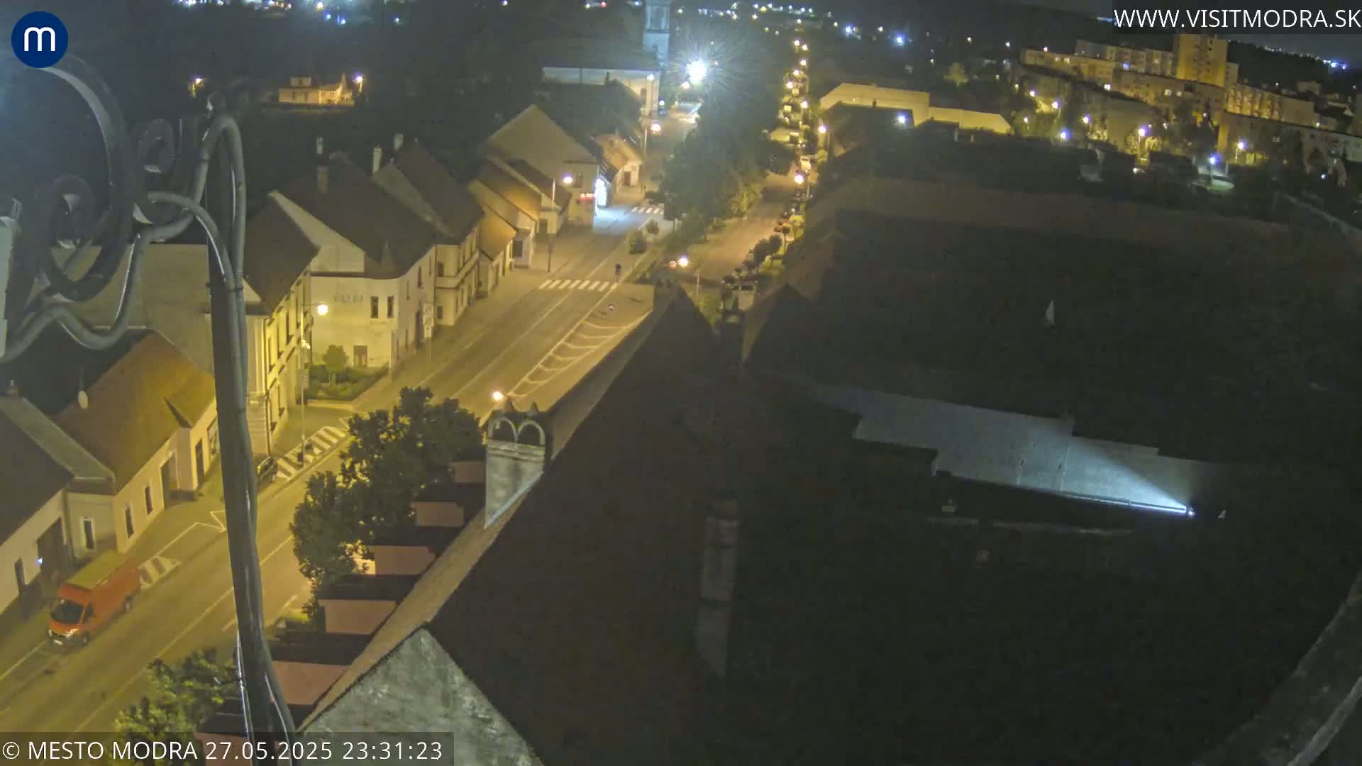 An aerial nighttime view of a town's street and buildings, illuminated by streetlights.
