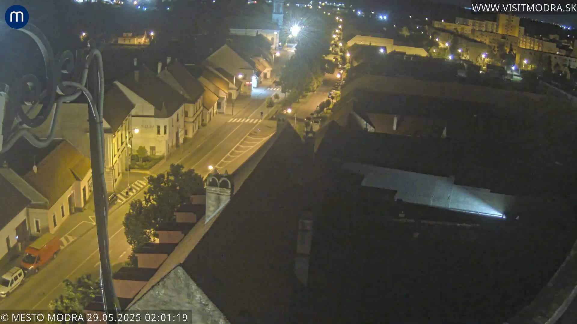 A nighttime, high-angle view shows a town's street lined with buildings, illuminated by streetlights.