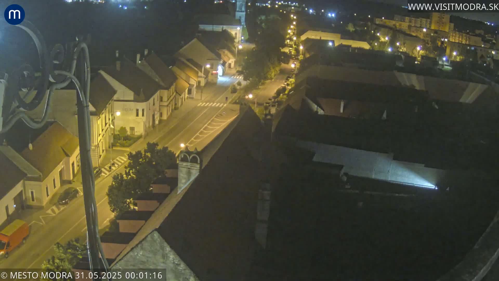 A nighttime high-angle view of a town's streets and buildings, illuminated by streetlights.
