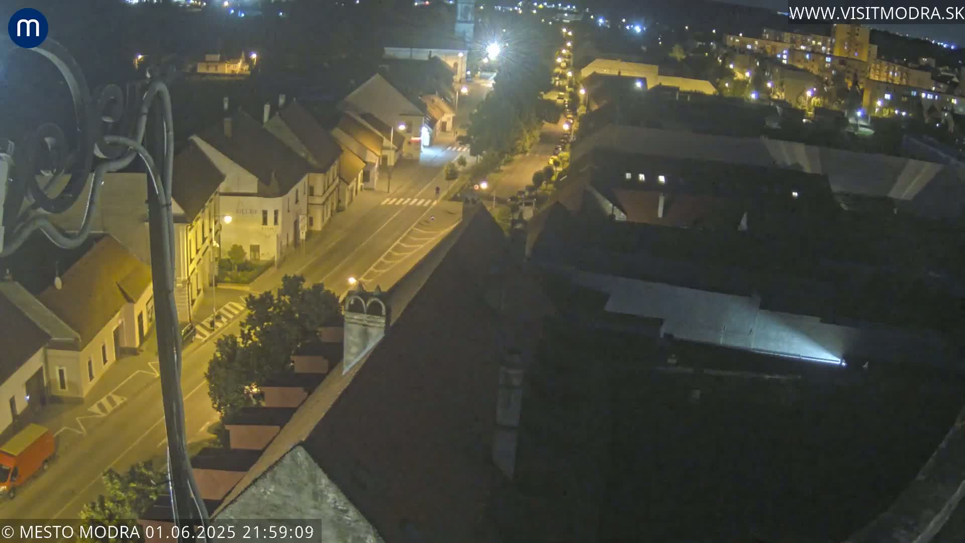 A nighttime high-angle view of a town's streets and buildings, illuminated by streetlights.
