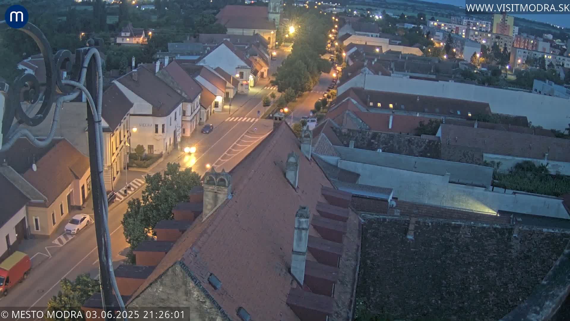 An aerial view at twilight shows a town's streets and buildings illuminated by streetlights.