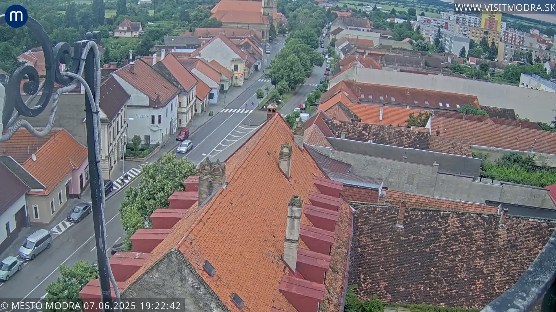 An elevated view shows a town's street and rooftops under a partly cloudy sky.