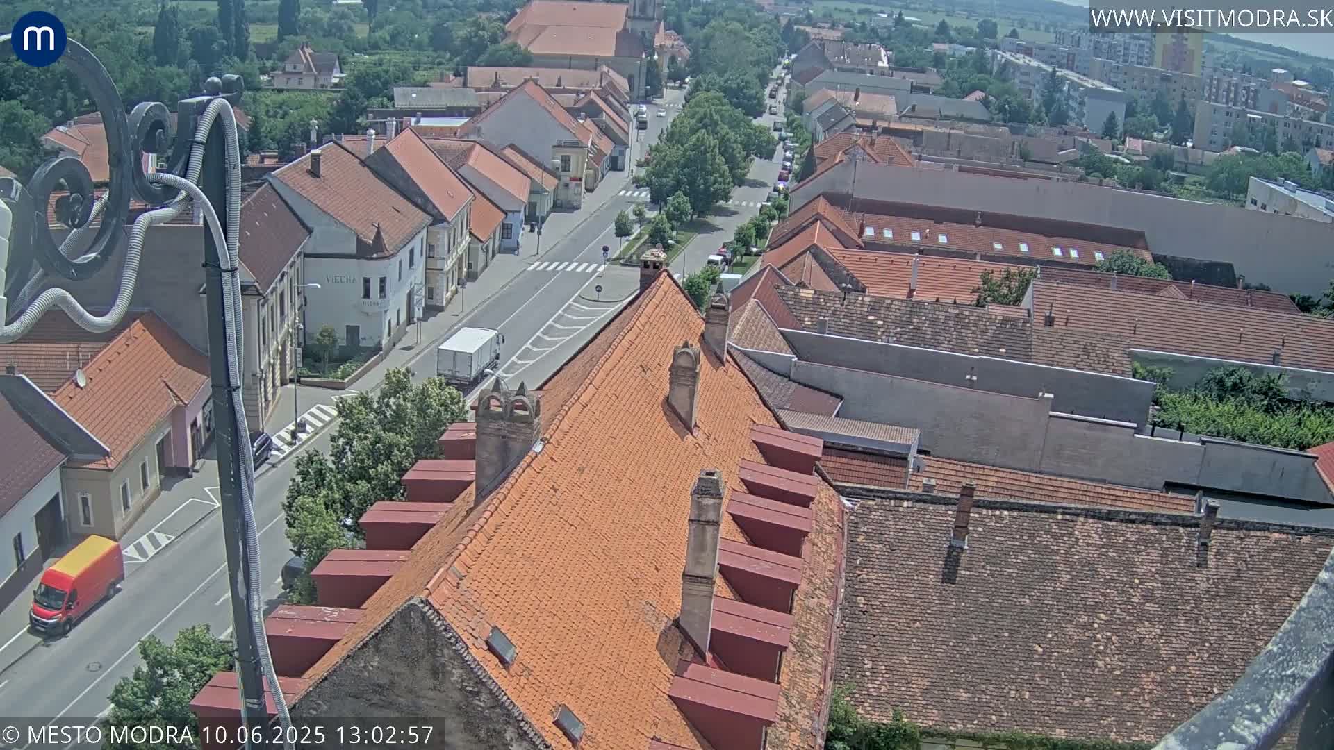 An aerial view shows a town's rooftops and a street on a sunny day.