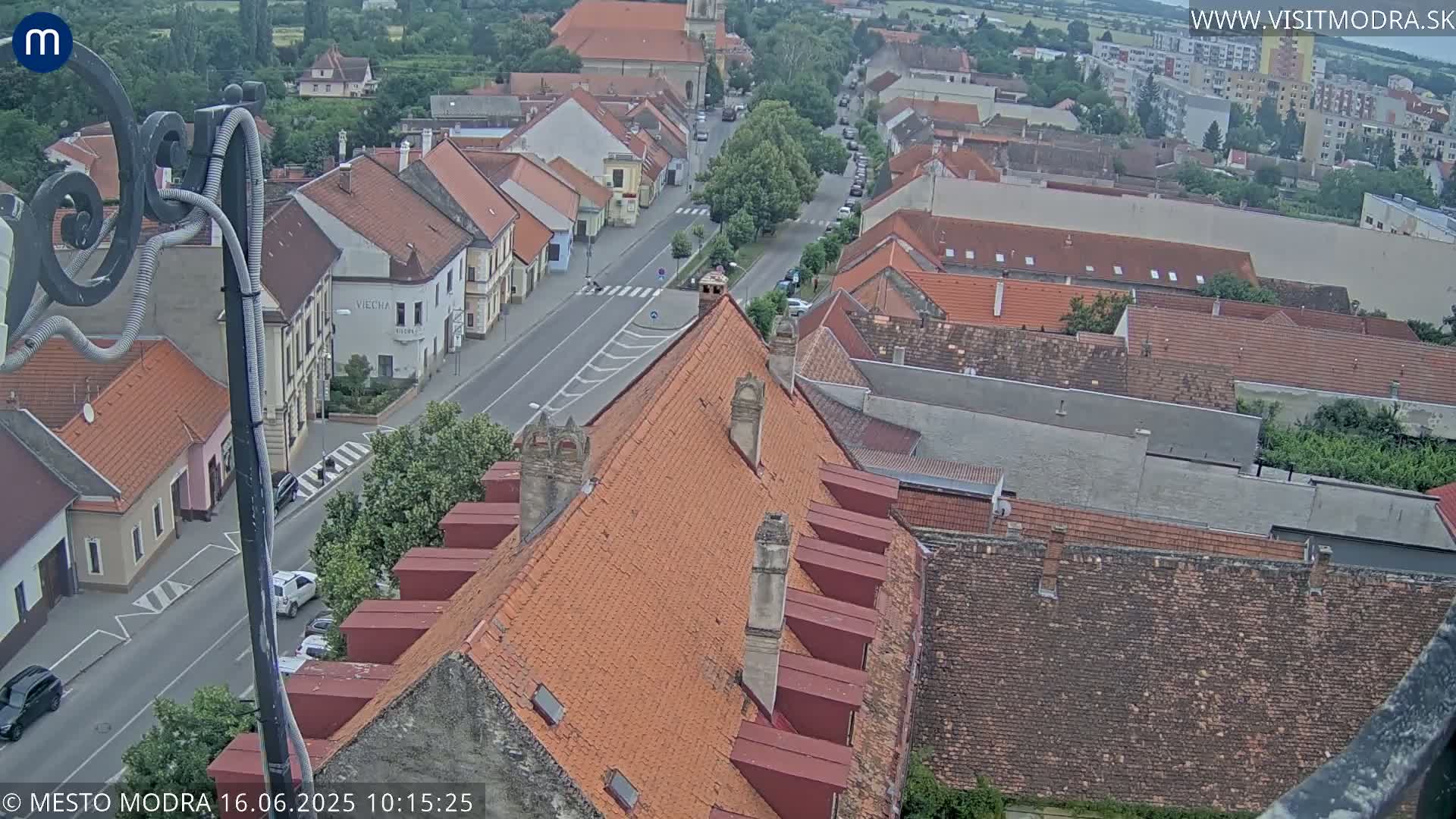An elevated view of a town on an overcast day, showing red-tiled rooftops and a street with cars.