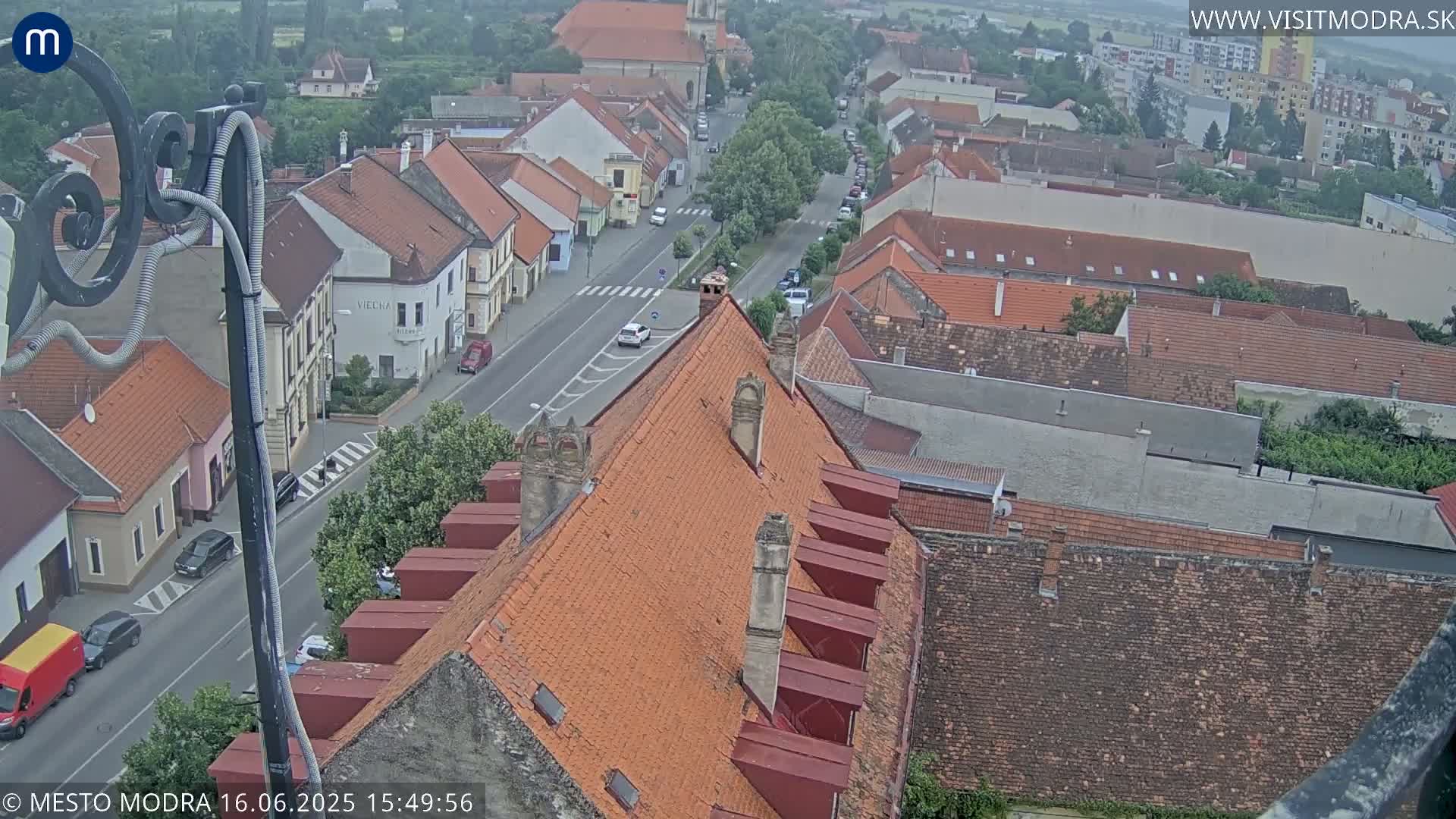 An elevated view of a town on an overcast day, showing a street with cars and numerous red-tiled rooftops.