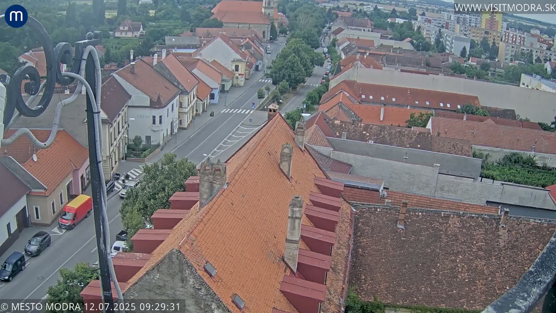 An elevated view of a town with red tile roofs and a street scene under partly cloudy skies.
