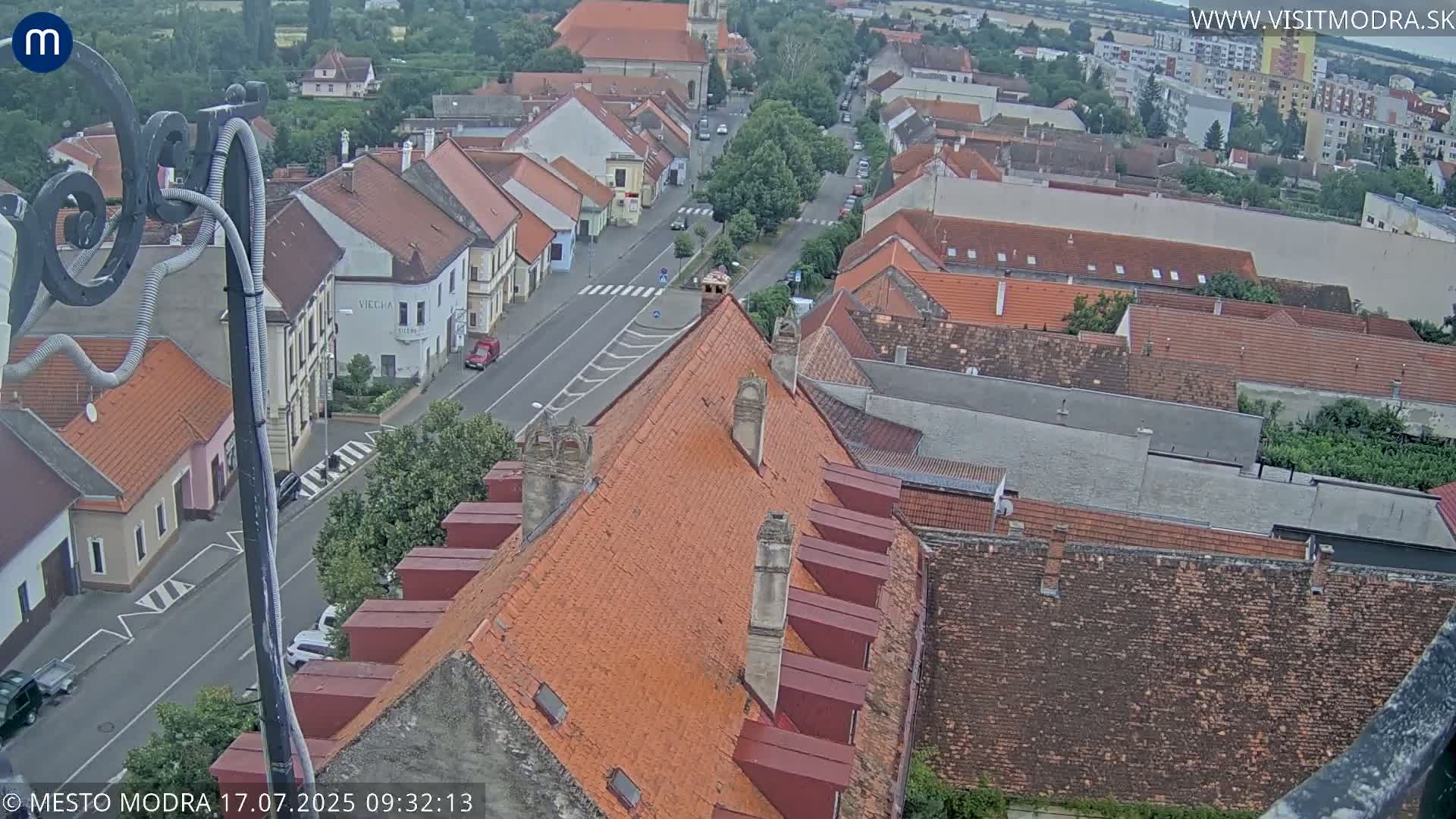 An elevated view shows a town with red-tiled roofs and a street running through it on an overcast day.