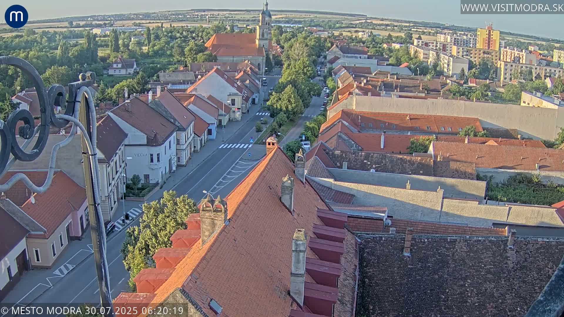 An elevated view shows a town with red-tiled roofs and a street running through it on an overcast day.