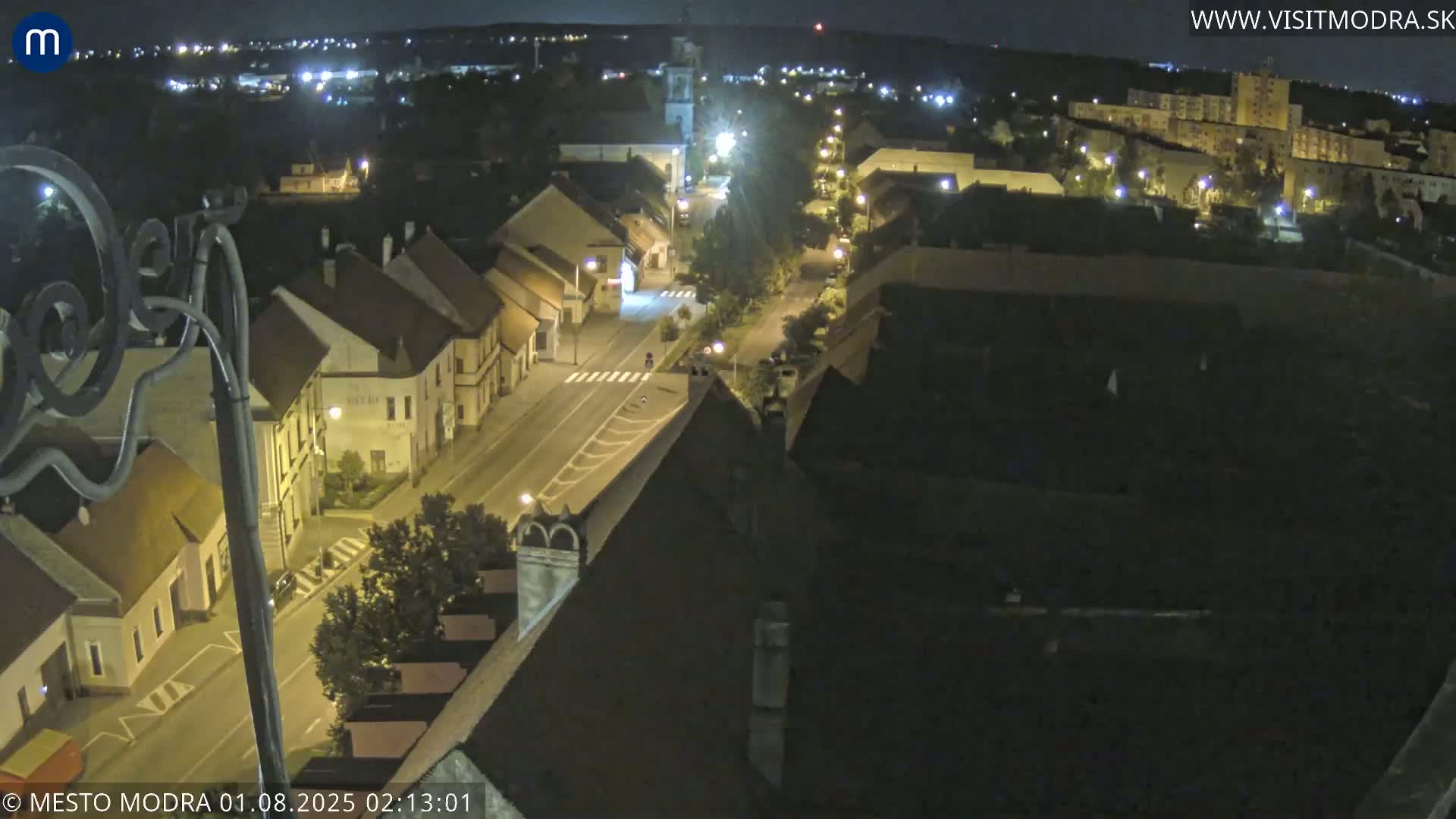 A nighttime aerial view of a town's street and buildings, illuminated by streetlights under a clear sky.