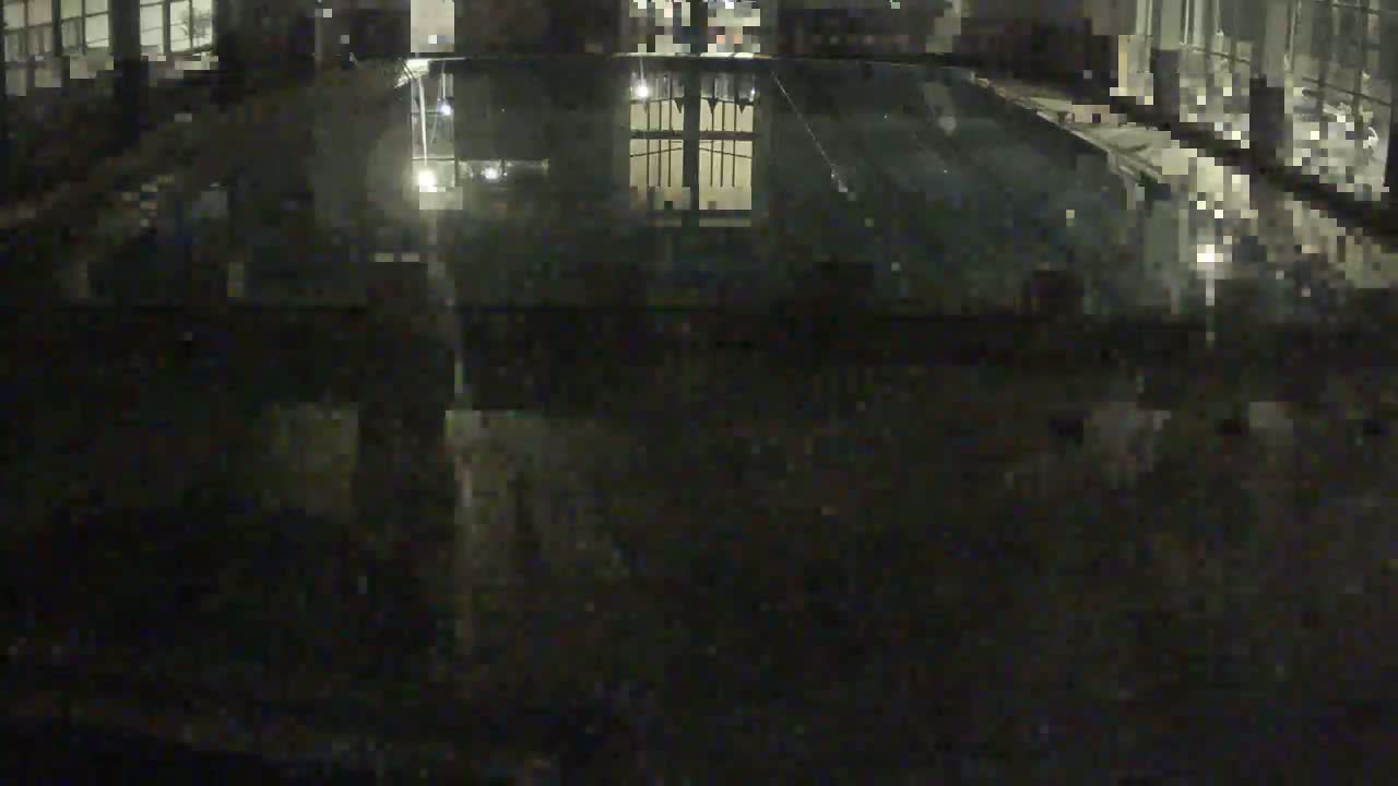 A dark, nighttime view of a reflective surface, possibly a pool or body of water, showing the reflection of a building's interior.