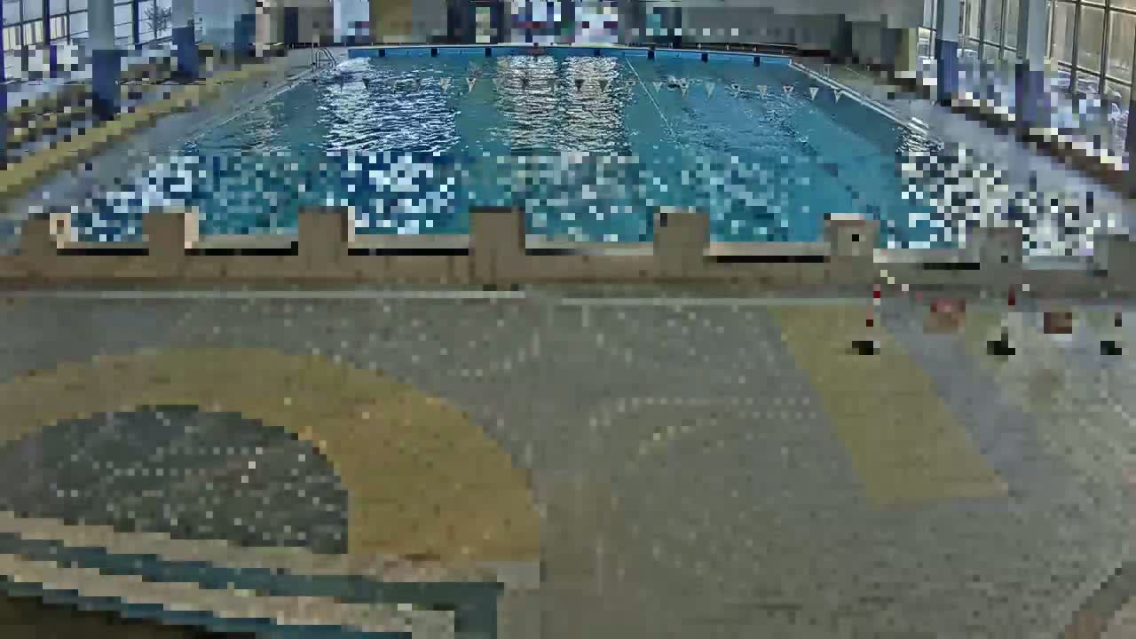 An indoor swimming pool with light-colored tiled flooring surrounding it.