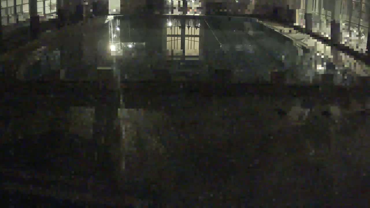 A dark, nighttime view of a reflective pool of water showing the reflection of a gated area and surrounding building.