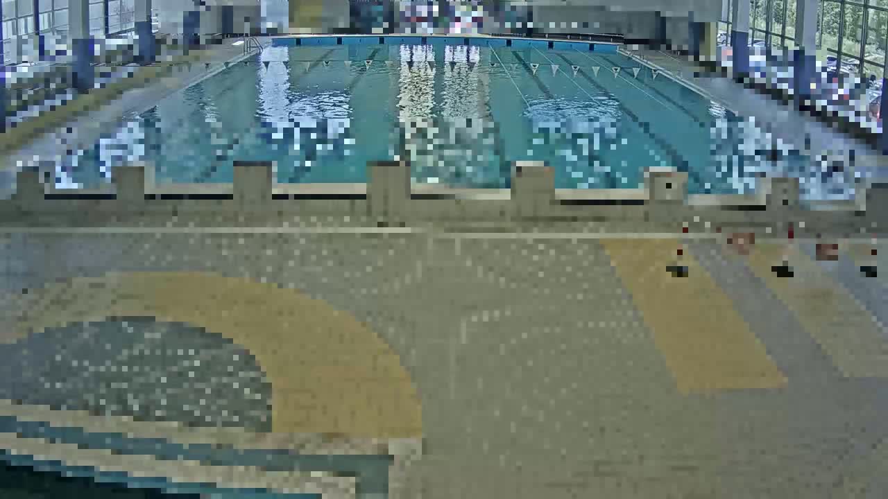 An indoor swimming pool with multiple lanes is shown, viewed from above, with a light-colored tiled area surrounding it.