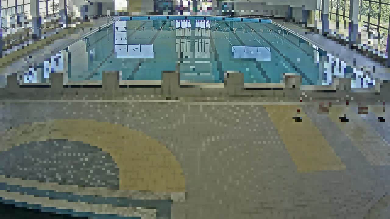 An indoor swimming pool with light-colored tiled flooring and several lane dividers is shown from an elevated vantage point.