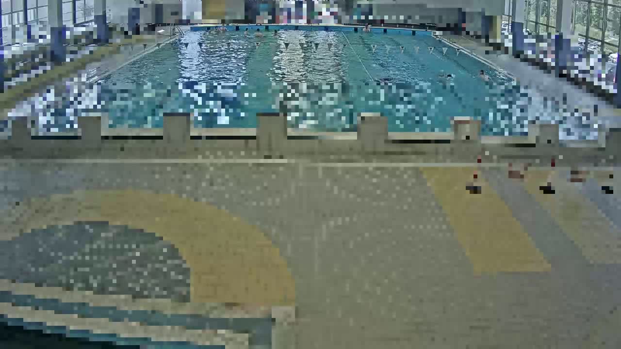 An indoor swimming pool with several people swimming and others sitting poolside.