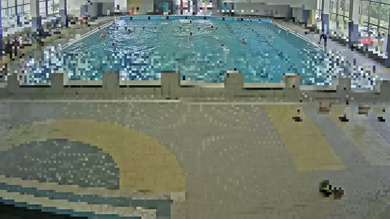 An indoor swimming pool with many people swimming in it, viewed from above.