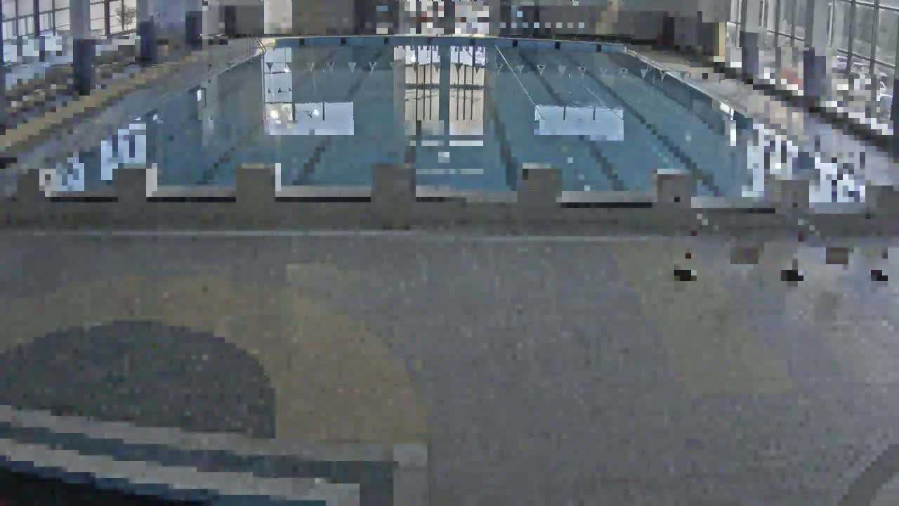 An indoor swimming pool is viewed from above, showing multiple lanes and a gray concrete deck.
