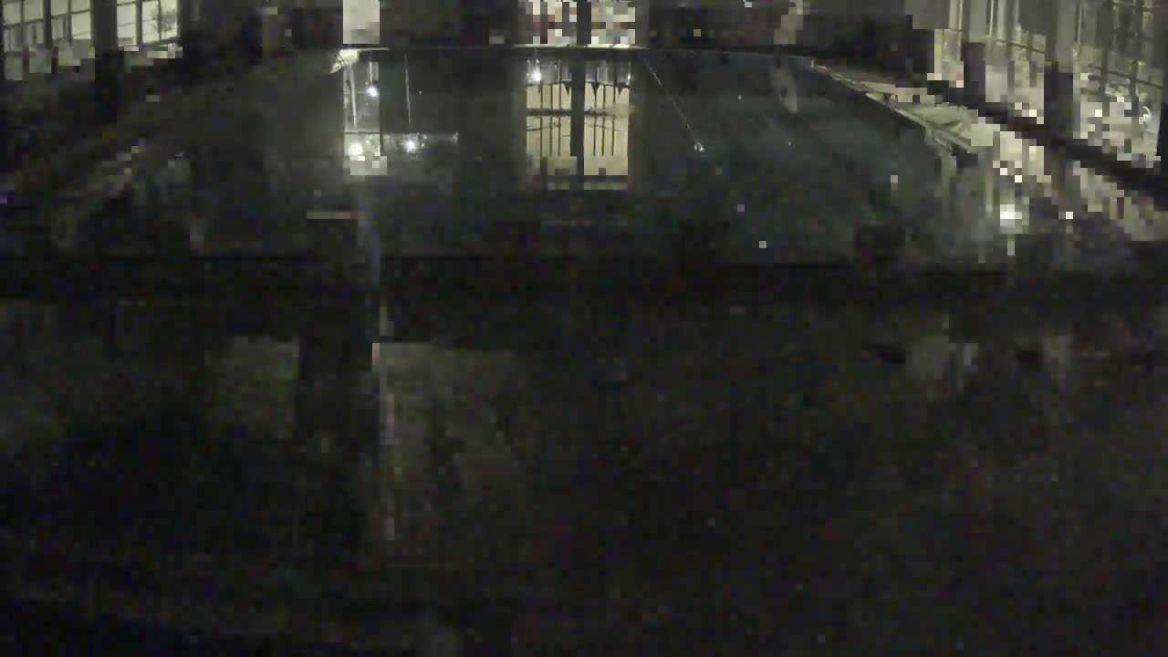 A dark, nighttime view shows a mostly empty, dark-colored pool reflecting lights from a building.
