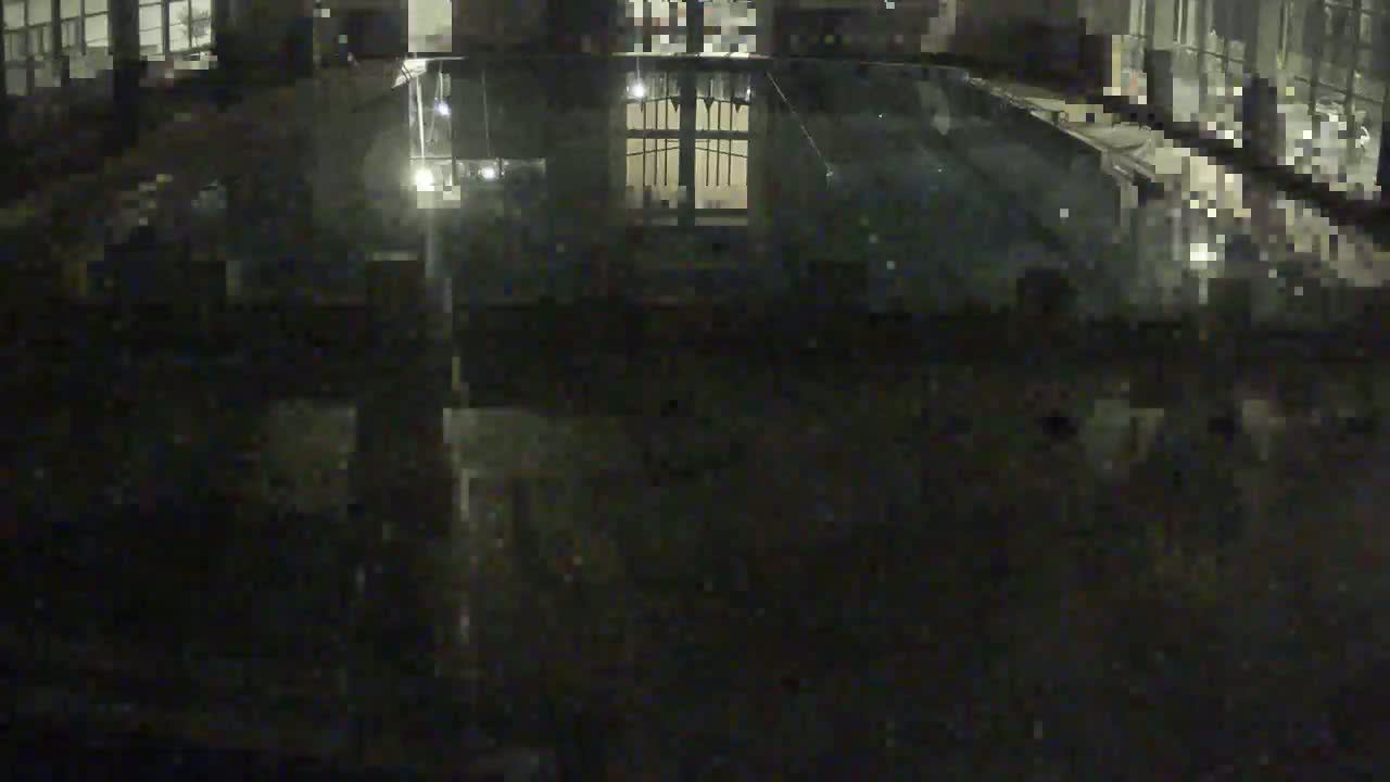 A dark, nighttime view shows a reflective, still body of water reflecting a building's lights and architecture.