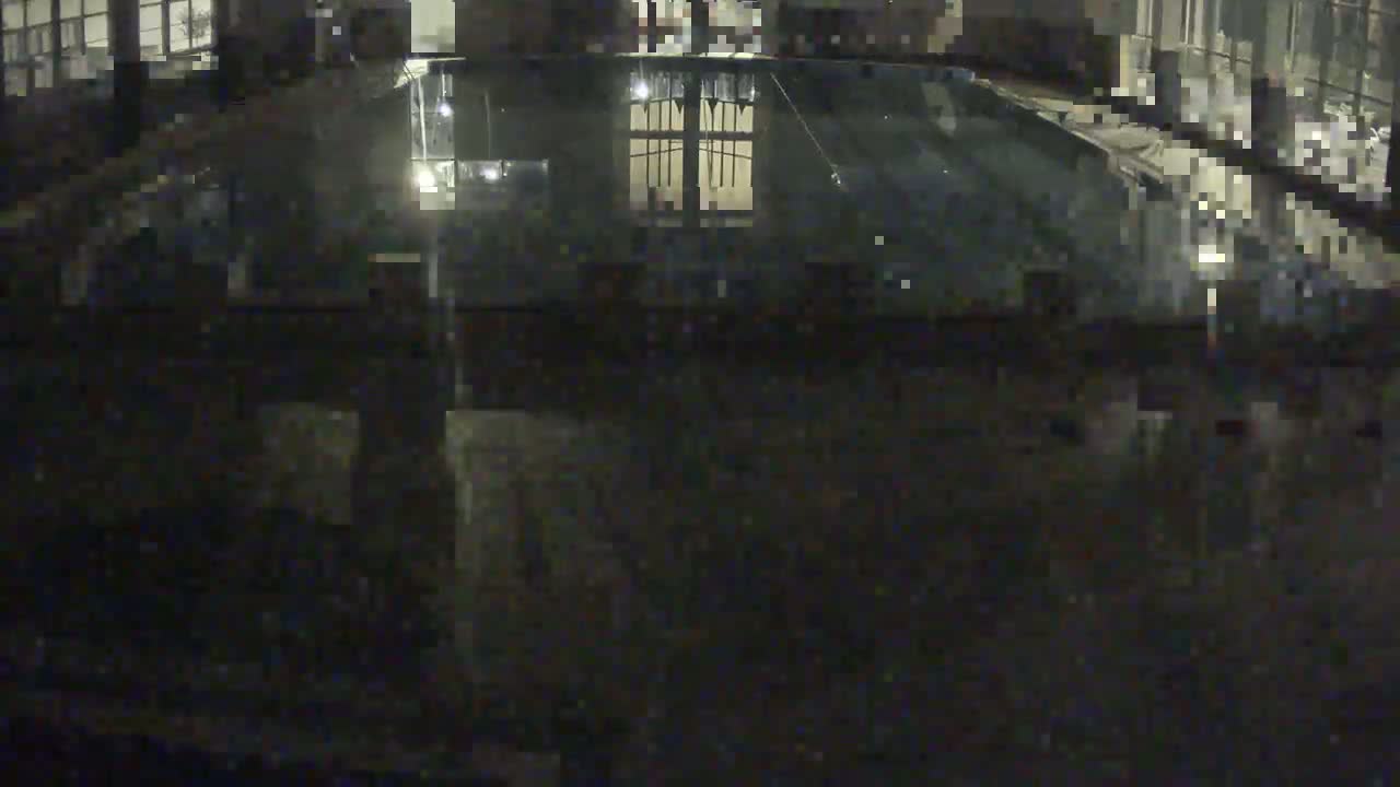 A dark, nighttime view of an indoor swimming pool reflecting nearby lights.