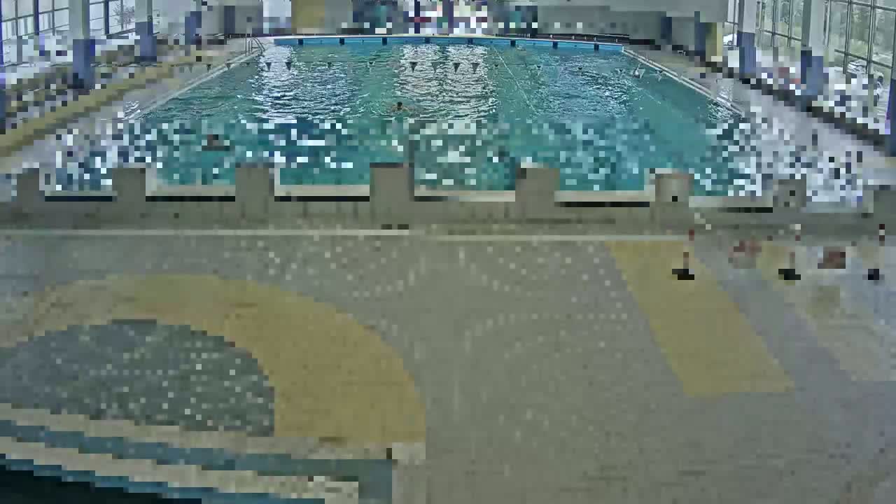 An indoor swimming pool with several people swimming, surrounded by a tiled floor and walls.