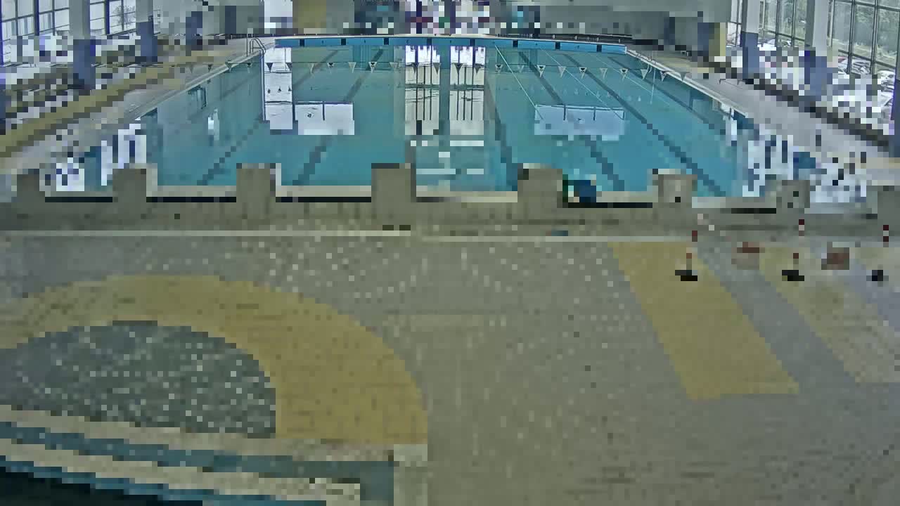 An indoor swimming pool with multiple lanes is visible from an elevated angle, the surrounding area appearing to be a tiled floor.