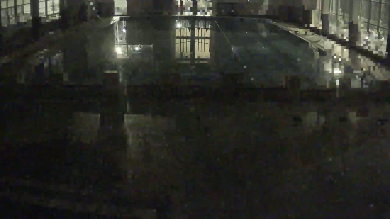 A dark, empty indoor swimming pool is reflected in the water at night.