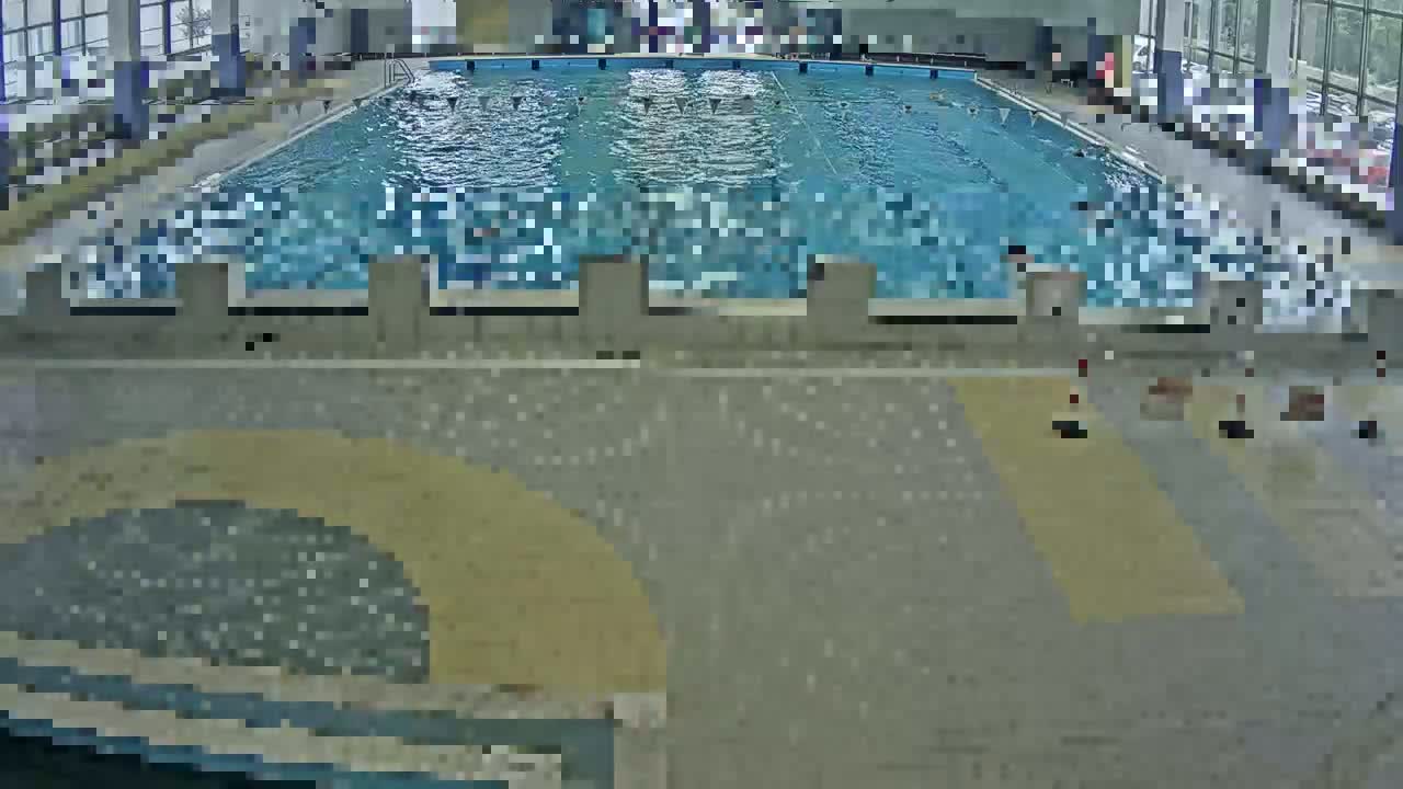 An indoor swimming pool with several people swimming and a few people standing around the pool deck.