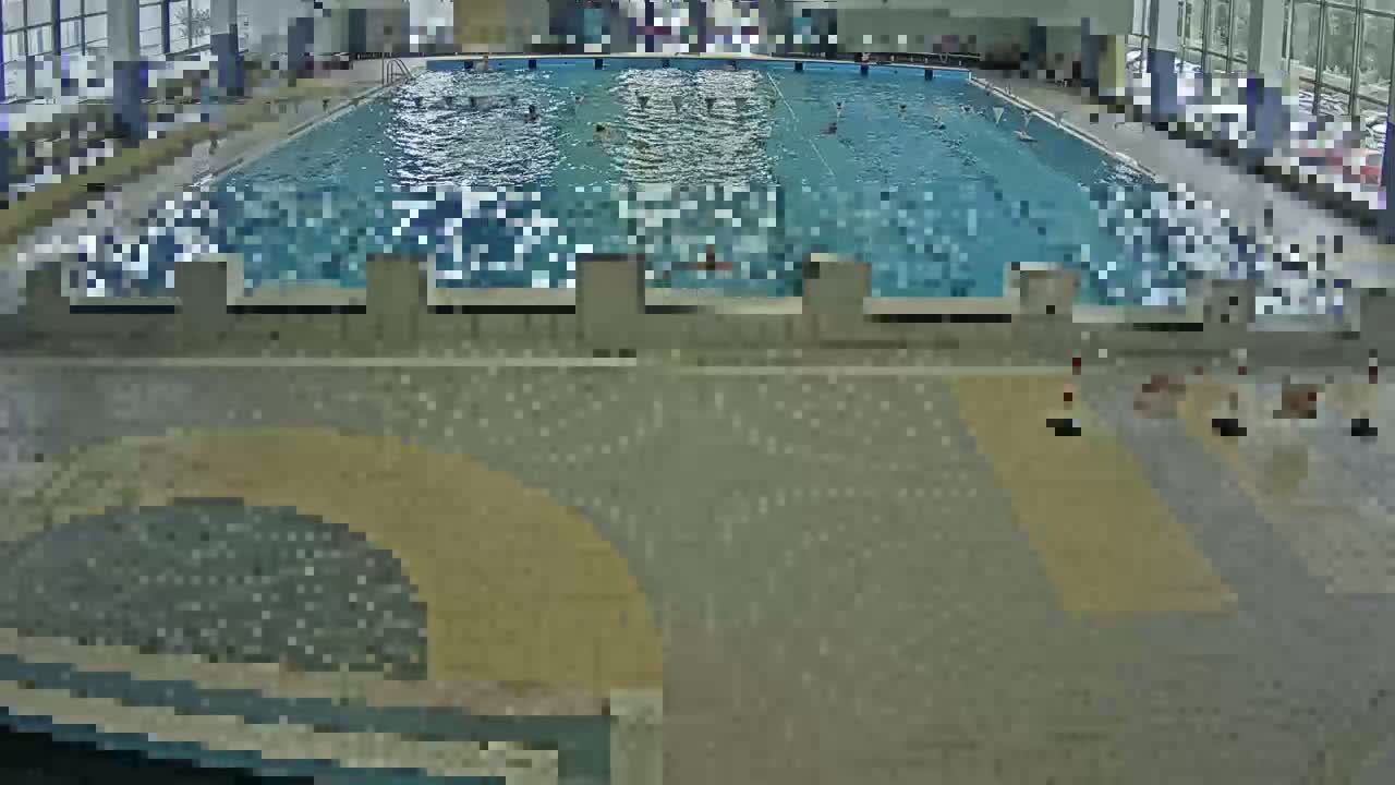 An indoor swimming pool with several people swimming and a few people sitting on the pool deck.