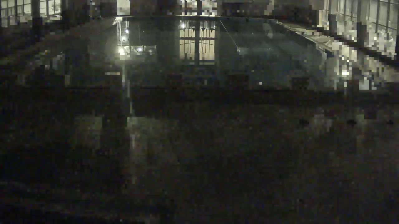 A dark, indoor view of a mostly empty swimming pool at night, reflecting interior lights.