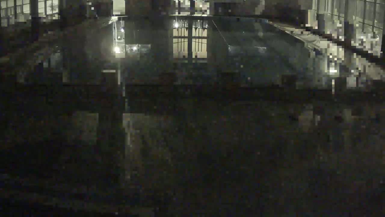 A dark, indoor swimming pool is reflected in the wet floor, illuminated by dim lighting.