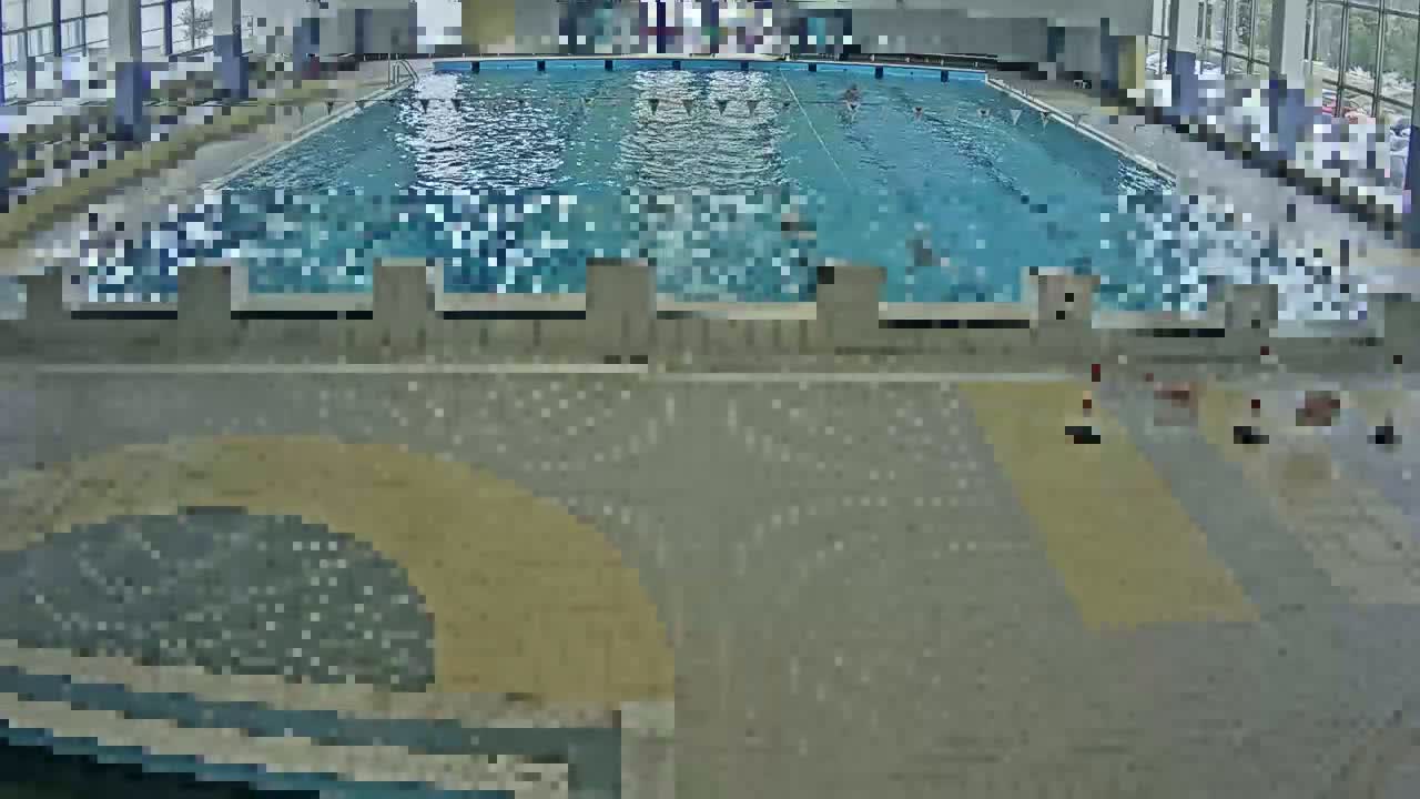 An indoor swimming pool with several people swimming and some people sitting on the pool deck.