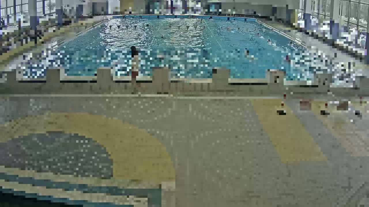 An indoor swimming pool with numerous people swimming and a few people standing near the edge.