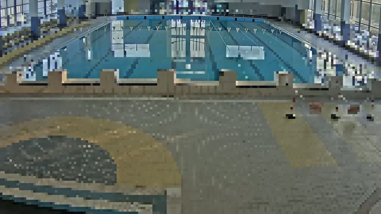 An indoor swimming pool is shown, with a large expanse of light grey tiled floor surrounding it.