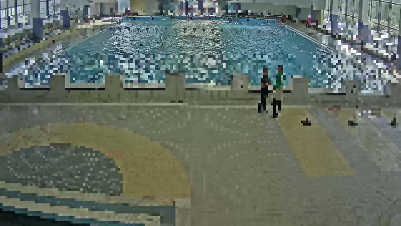 An indoor swimming pool with many people swimming and a few people standing poolside.