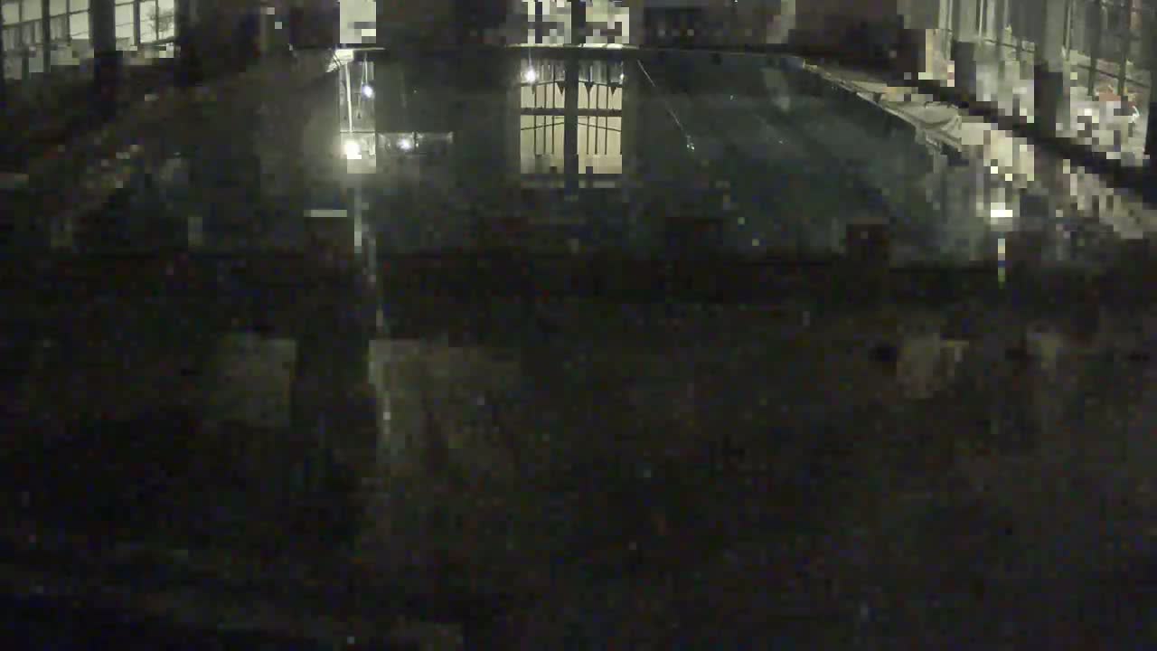 A dark, nighttime view of a mostly empty indoor swimming pool reflecting nearby windows.