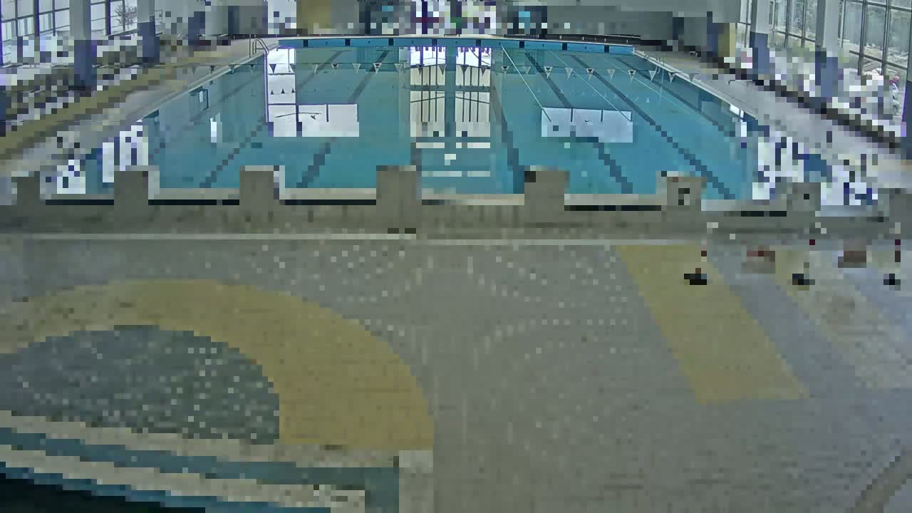 An indoor swimming pool with multiple lanes and surrounding tiled floors is seen from an elevated view.