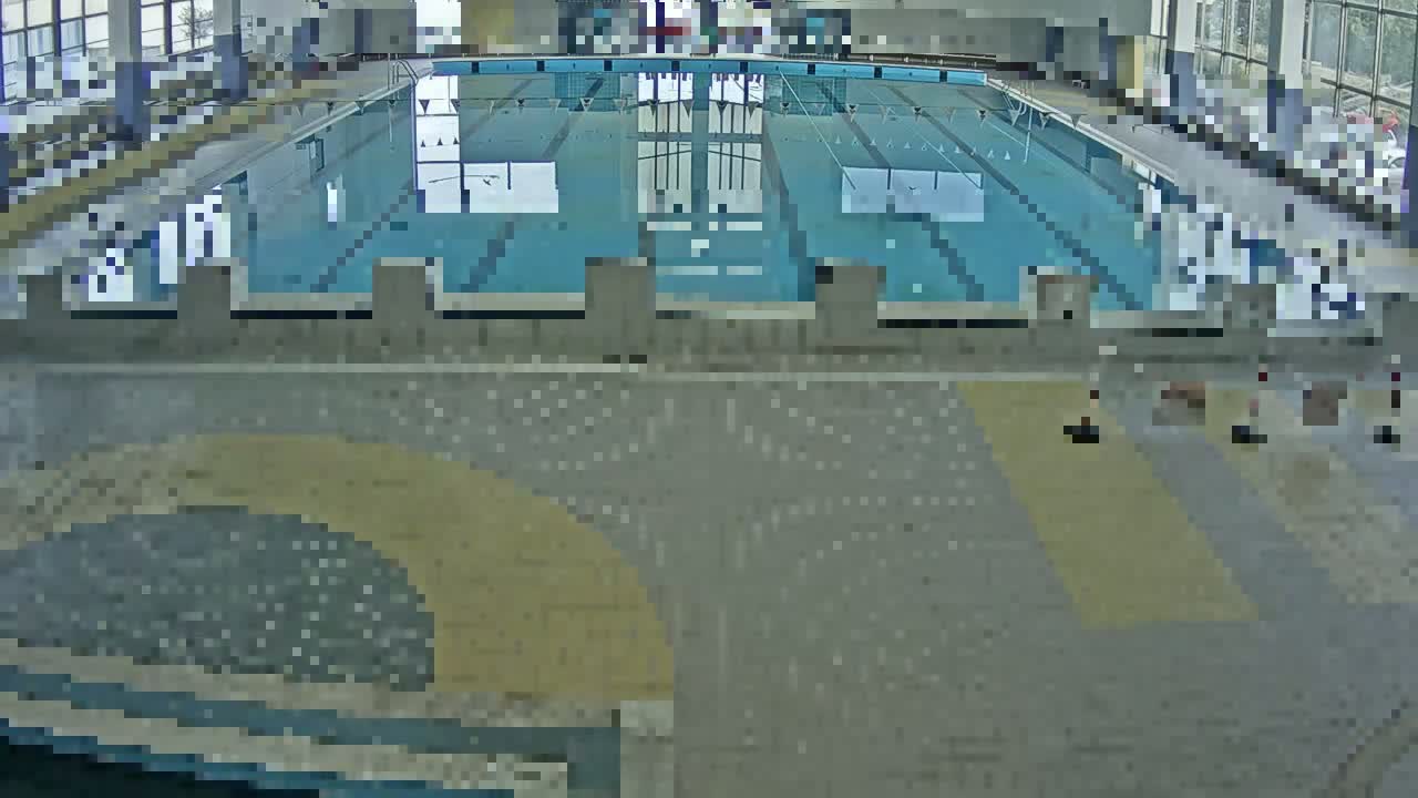 An indoor swimming pool with several lanes is viewed from above, and the surrounding floor is mostly gray.