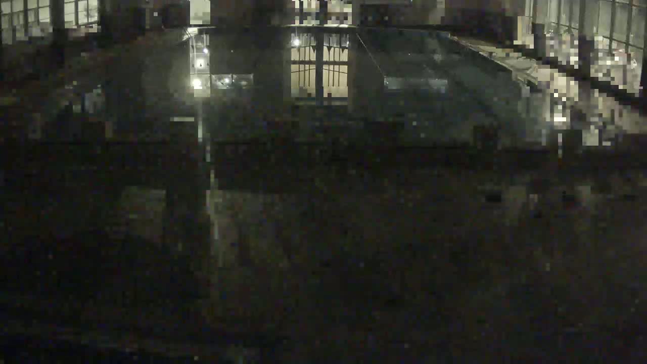 A dark, indoor swimming pool is seen at night, reflecting the lights and windows of the building.